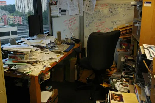 A messy desk with a whiteboard and piles of papers and disks that need a desk organizer.